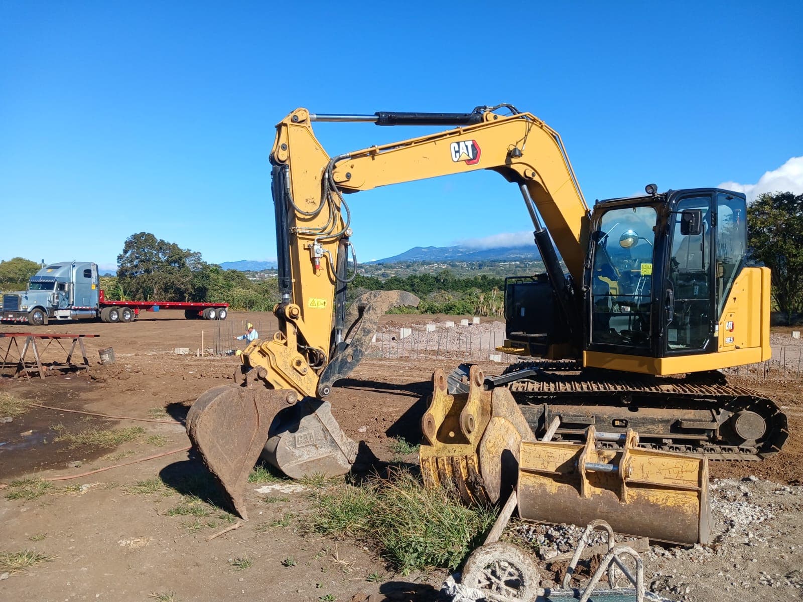 Excavadora CAT 307.5 en un terreno, con un cabezal azul al fondo